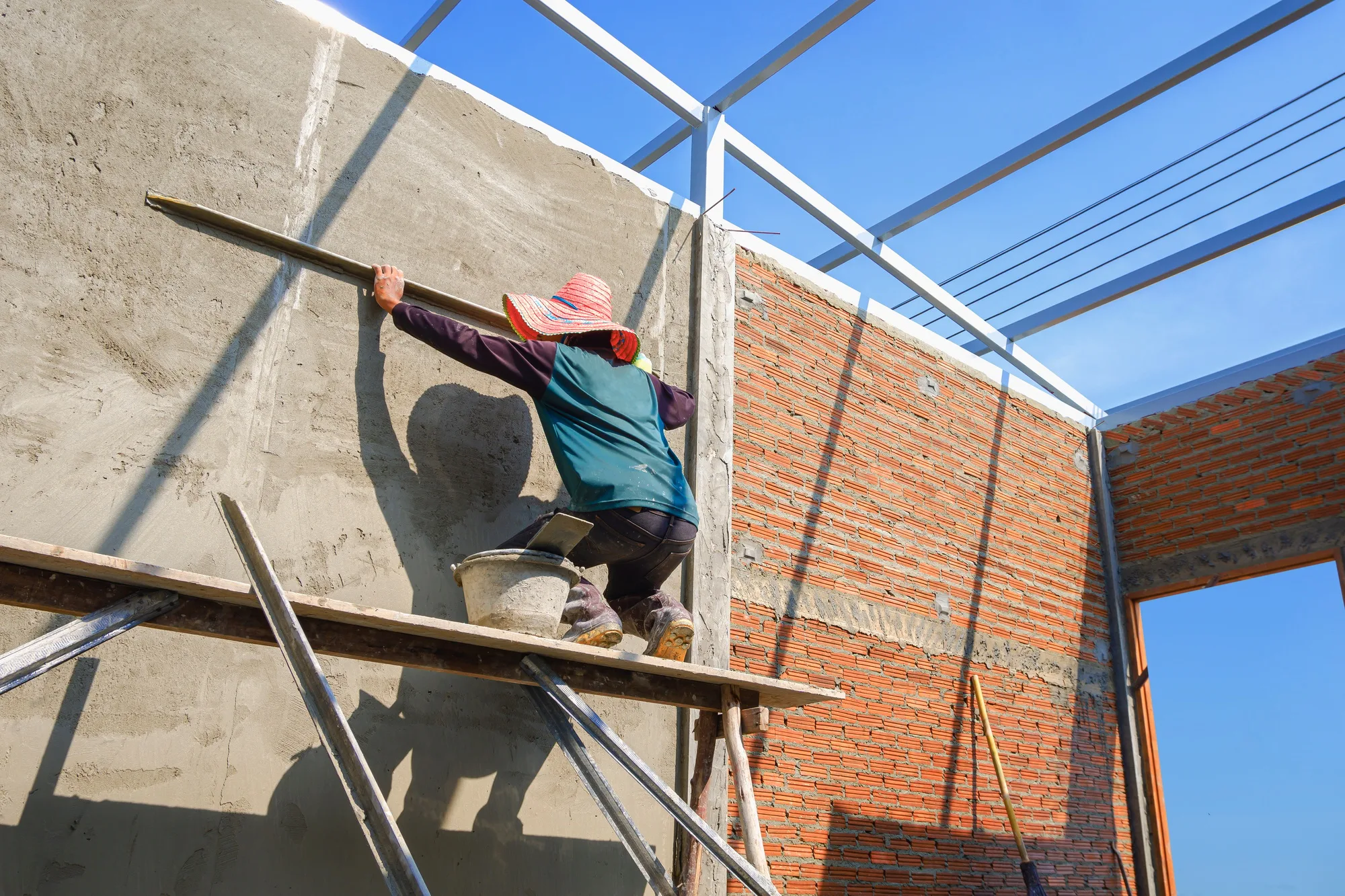 Asian builder worker on wooden scaffolding is polishing concrete wall in house construction site